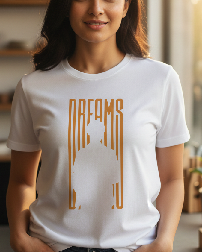 Woman wearing a white t-shirt with a gold Buddha silhouette and 'DREAMS' text in a home setting.