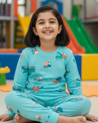 Young girl in a teal outfit with vehicle patterns sitting in an indoor playground.