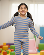 Young girl in blue and beige striped pajamas standing in a colorful indoor play area.