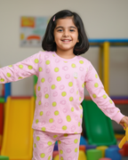 Young girl in pink pajamas with a pattern, standing in a colorful indoor play area.