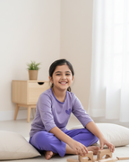 Young girl playing with wooden blocks on a light-colored floor.