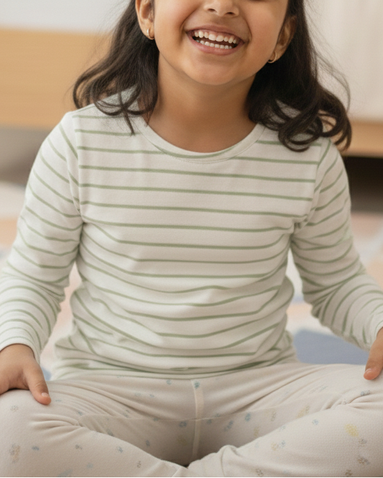 Young girl sitting on a colorful rug in a bedroom wearing striped pajamas.