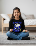 Young girl sitting on a rug wearing a black shirt with Snoopy and text, in a room with a couch and pillows.