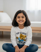 Young girl sitting on the floor wearing a 'Top Scorer' shirt with a teddy bear graphic.