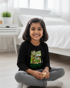 Young girl sitting on the floor wearing a black shirt with a colorful design and gray pants.