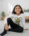 Young girl sitting on the floor wearing a white long-sleeve shirt with a colorful graphic design.