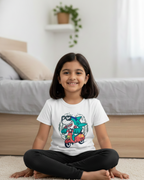 Young girl sitting on the floor wearing a white t-shirt with a colorful graphic design.