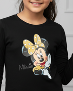 Young girl wearing a black long-sleeve shirt with a Minnie Mouse design, standing against a white wall.