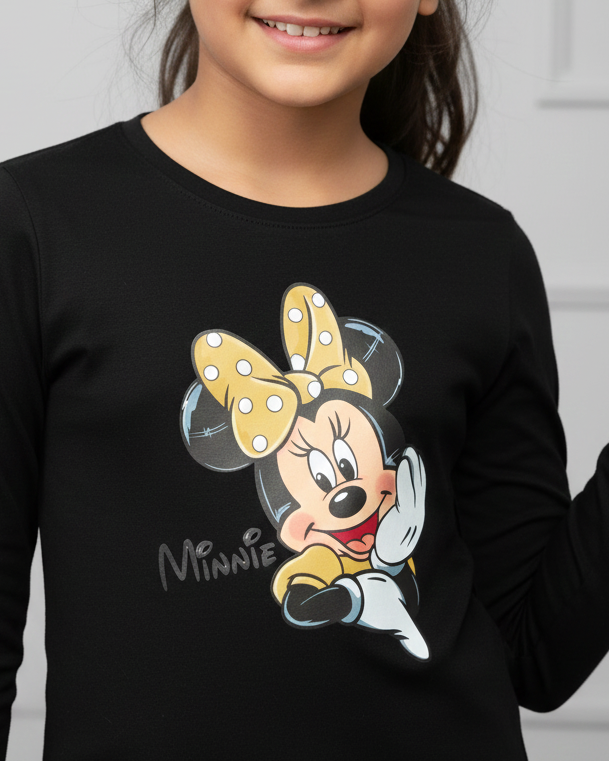 Young girl wearing a black long-sleeve shirt with a Minnie Mouse design, standing against a white wall.