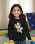 Young girl wearing a black long-sleeve shirt with a cartoon character, standing in a colorful playroom.