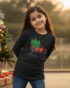 Young girl wearing a black sweater with a Christmas design, standing in front of a decorated tree and presents.