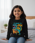 Young girl wearing a black sweatshirt with a colorful dinosaur graphic and text, sitting on a bed.