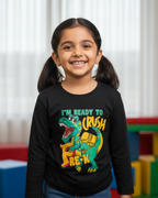 Young girl wearing a black t-shirt with a dinosaur graphic and text, standing in front of colorful blocks.