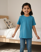 Young girl wearing a blue t-shirt and jeans standing in a bedroom.