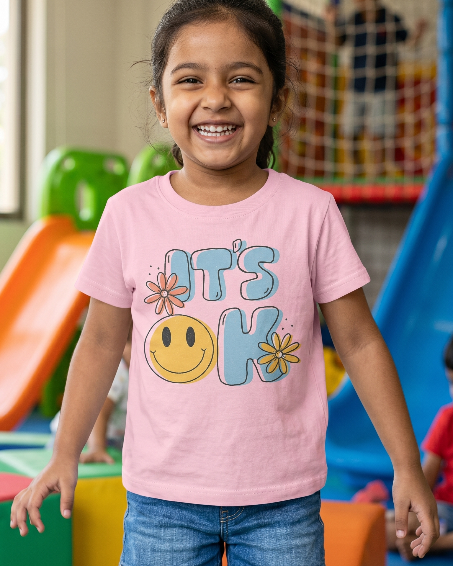 Young girl wearing a pink t-shirt with a smiley face and text in a colorful playground.