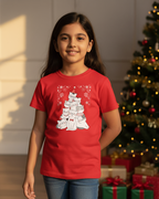 Young girl wearing a red t-shirt with a graphic design, standing in front of a decorated Christmas tree and presents.