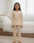 Young girl wearing beige pajamas standing in a bedroom.