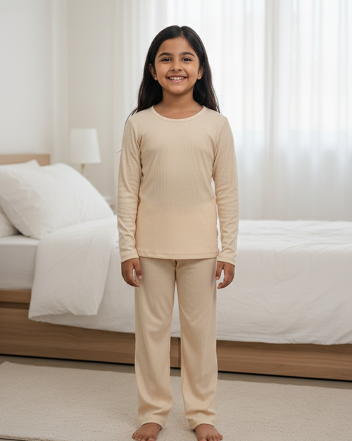 Young girl wearing beige pajamas standing in a bedroom.